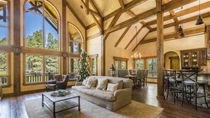 A spacious living room with a large window, a sofa, and a coffee table. - Luxury | Golf Course View | 18th Overlook (Angel Fire)