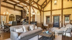 A spacious living room with a large sofa, a coffee table, and a fireplace. There is a dining area with a table and chairs, and a kitchen in the background. - Luxury | Golf Course View | 18th Overlook (Angel Fire)