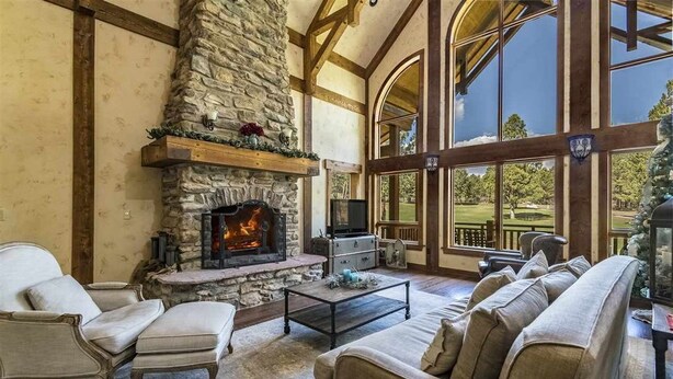 A cozy living room with a stone fireplace, comfortable seating, and large windows offering a view of the outdoors. - Luxury | Golf Course View | 18th Overlook (Angel Fire)