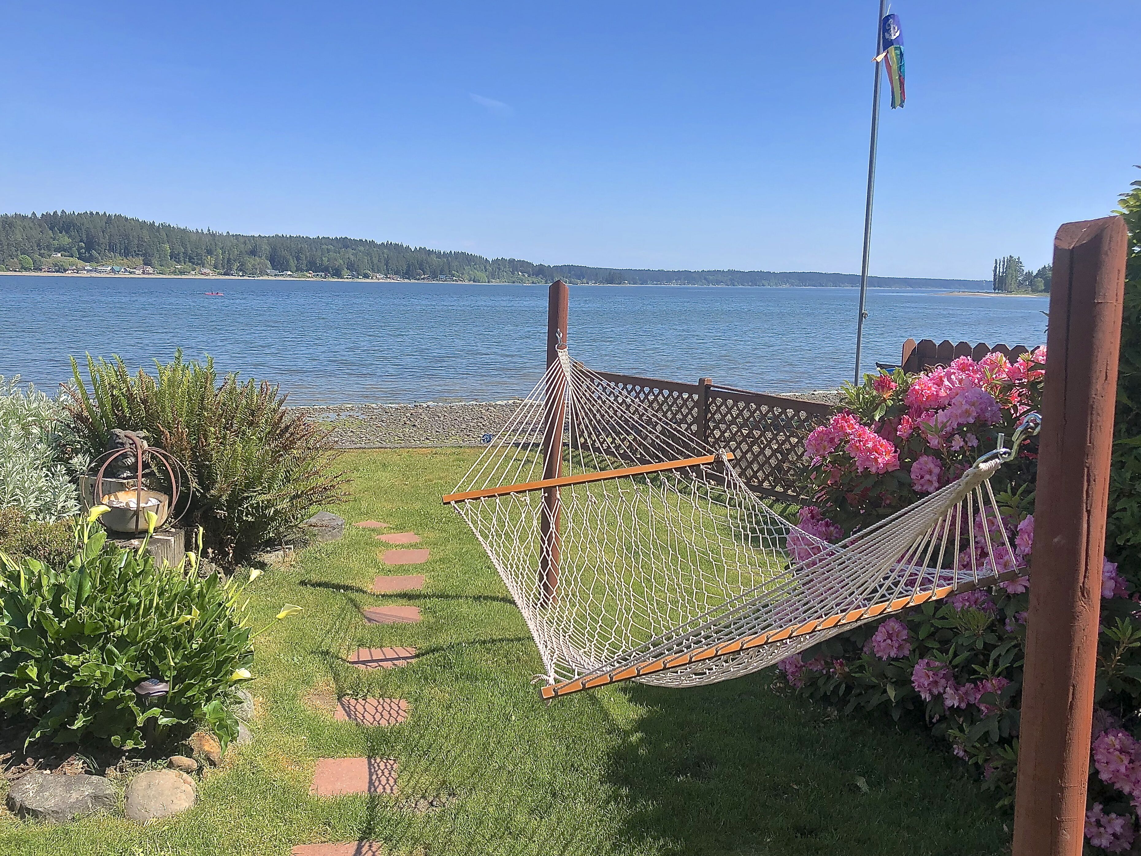 A hammock in a garden with a view of a lake and a flag.
