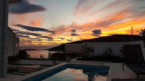 Une piscine offrant une vue sur le coucher de soleil au-dessus d’une étendue d’eau et d’un paysage vallonné.