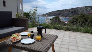 Un espace de restauration en plein air avec une table en osier, des assiettes remplies de nourriture, des verres et une cafetière.