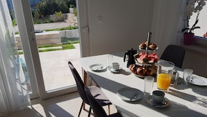 Une table à manger dressée avec des assiettes, des tasses, un pichet de jus d’orange et un présentoir à gâteaux à plusieurs niveaux.
