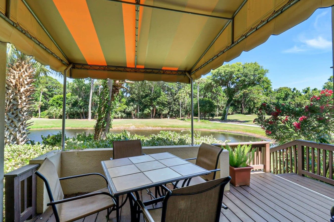 A covered outdoor seating area with a table and chairs, overlooking a golf course and a pond.