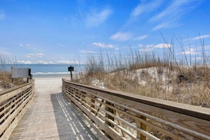 A wooden boardwalk leading to a beach with a clear sky.