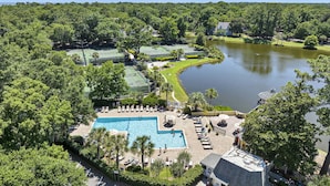 Een resort met een zwembad, tennisbanen en een meer.