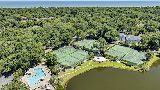 Luchtbeeld van een woongebied met meerdere tennisbanen, een zwembad en een groot waterlichaam.