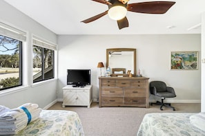 Une chambre à coucher comprenant un lit, une commode, un téléviseur, un bureau et un ventilateur de plafond.