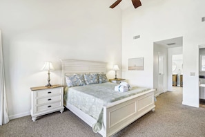 A bedroom with a bed, two bedside tables, a nightstand, a ceiling fan, and a door leading to another room.
