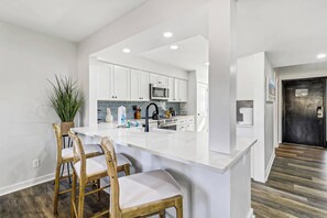A modern kitchen with white cabinets, a black faucet, and a bar area with two wooden chairs. - Inverness Villa on Golf Course with Pool & Tennis (Hilton Head Island)