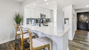 A modern kitchen with white cabinetry, a central island with chairs, a microwave, and a sink. - Inverness Villa on Golf Course with Pool & Tennis (Hilton Head Island)