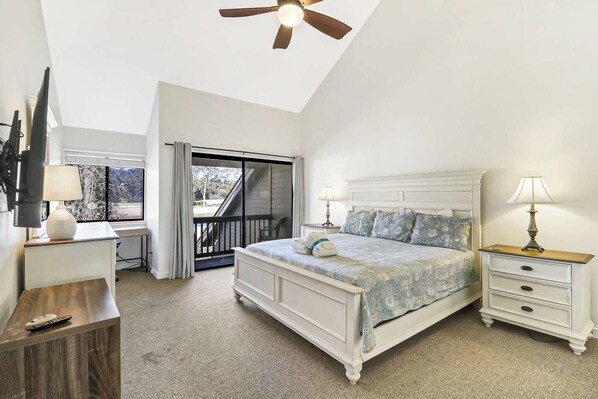 A bedroom with a bed, bedside tables, a desk, a ceiling fan, and a view through a sliding door to an outdoor area.