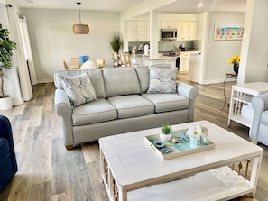 A modern living room with a sofa, coffee table, and a kitchen in the background.