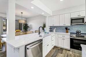 A modern kitchen with white cabinetry, a built-in dishwasher, a stainless steel oven, and a microwave.