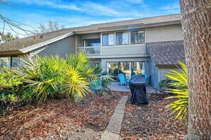 A two-story house with a patio area, a covered barbecue grill, and a variety of plants.
