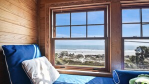 Una stanza con una grande finestra vista spiaggia, un letto con biancheria azzurra e bianca, e un muro in legno.