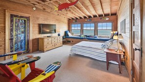 Camera da letto in una baita di legno, con un letto, TV, cassettiera e finestre con vista sul mare.