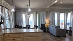 Un vaste espace de vie comprenant un grand îlot central, un canapé gris et une table à manger.