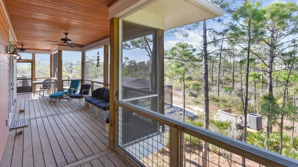 Eine Holzterrasse mit Außenmöbeln, einem Deckenventilator und Blick auf eine bewaldete Gegend.