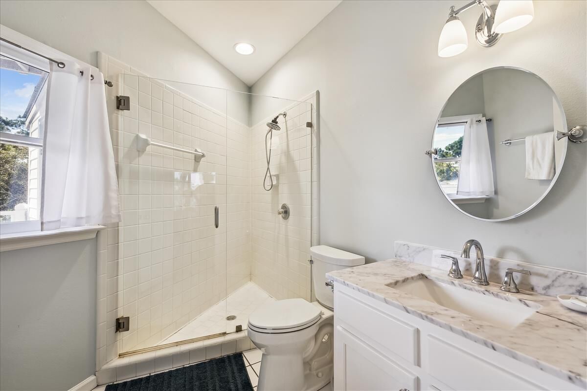 Un baño moderno con ducha de vidrio, inodoro, lavamanos con encimera de mármol y un espejo grande.