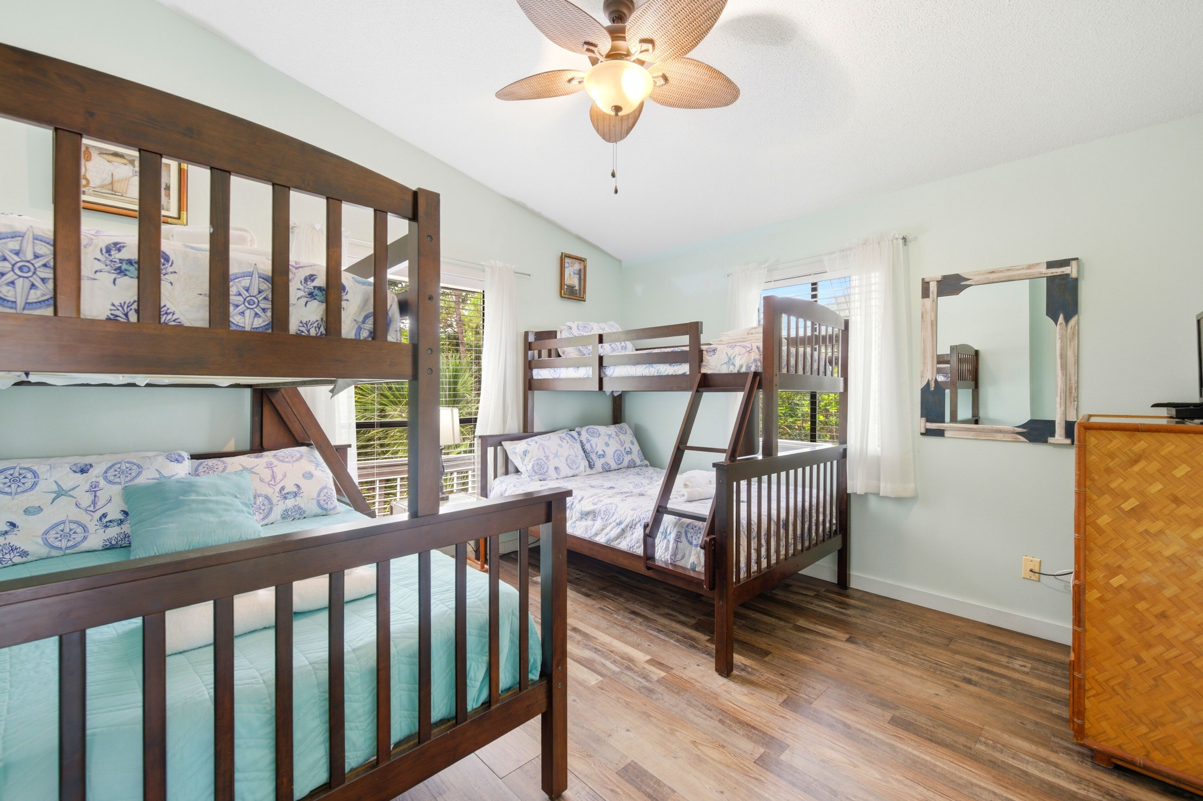A room with bunk beds, a ceiling fan, a wooden floor, and a window with curtains.