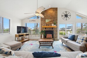 A living room with a television, a fireplace, a ceiling fan, and a large window.