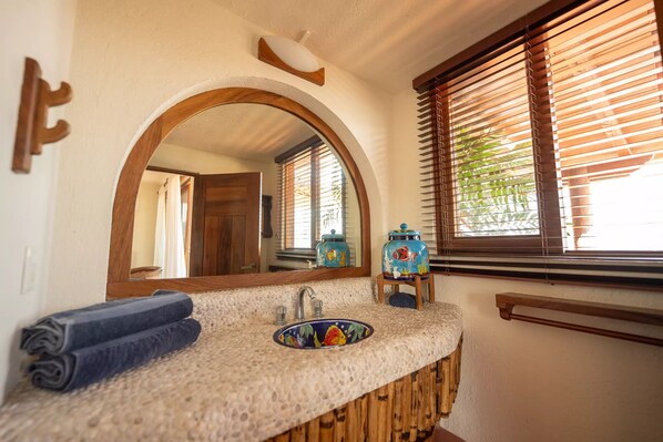 A bathroom with a round mirror, wooden vanity, and a sink with a decorative tile backsplash. - Amazing views of La Ropa Bay 3 BR condo (Zihuatanejo)