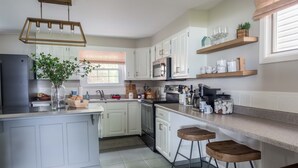 A modern kitchen with white cabinets, a central island with stools, a built-in oven, and a coffee machine. - Lakefront Renovated 4BR w/ Dock, Kayaks, Walk to Bemus Point (Bemus Point)