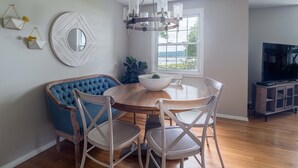 A dining area with a round table, blue upholstered chairs, and a white bowl. - Lakefront Renovated 4BR w/ Dock, Kayaks, Walk to Bemus Point (Bemus Point)