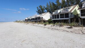 Reihenweise Strandhäuser mit Balkonen, ein Sandstrand im Vordergrund und Bäume im Hintergrund.