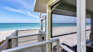 Blick auf den Strand von einem Balkon mit Metallgeländer und Glastür.