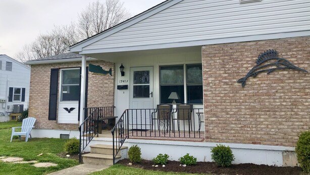 A single-story house with a brick facade, a front porch with a bench, and a mailbox. - Cozy Beach Cottage in Island’s residential neighborhood! (Cape May)