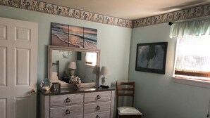 A bedroom with a bed, dresser, chair, and a painting above the dresser. - Cozy Beach Cottage in Island’s residential neighborhood! (Cape May)