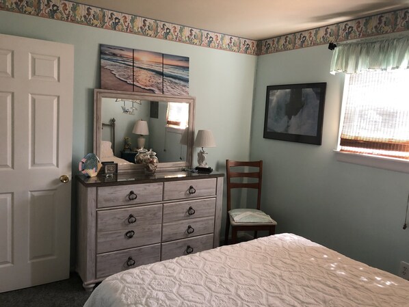 A bedroom with a bed, dresser, chair, and a painting above the dresser.