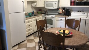 A kitchen with white cabinets, a microwave, stove, and a dining table with chairs. - Cozy Beach Cottage in Island’s residential neighborhood! (Cape May)