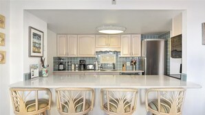 A kitchen with white cabinets, a central island with bar stools, and a stainless steel refrigerator. - 93rd St , 3br/2ba oceanside view in oceanfront bldg Occ 8 (Ocean City)