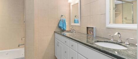 Une salle de bain moderne avec des carreaux de couleur beige, un grand miroir, une baignoire et un meuble-lavabo doté d’un évier et de deux robinets.