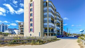 A multi-story hotel with balconies, located near a beach with a wooden fence and a water tower in the background. - 93rd St , 3br/2ba oceanside view in oceanfront bldg Occ 8 (Ocean City)