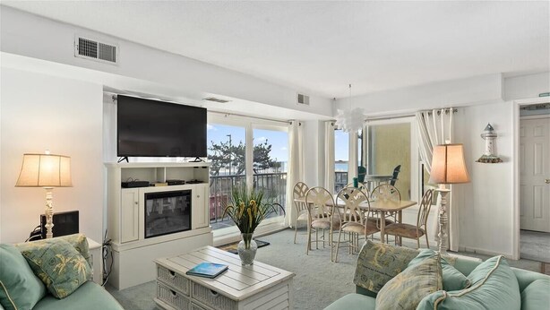 A living room with a TV, sofa, coffee table, and a balcony with chairs. - 93rd St , 3br/2ba oceanside view in oceanfront bldg Occ 8 (Ocean City)