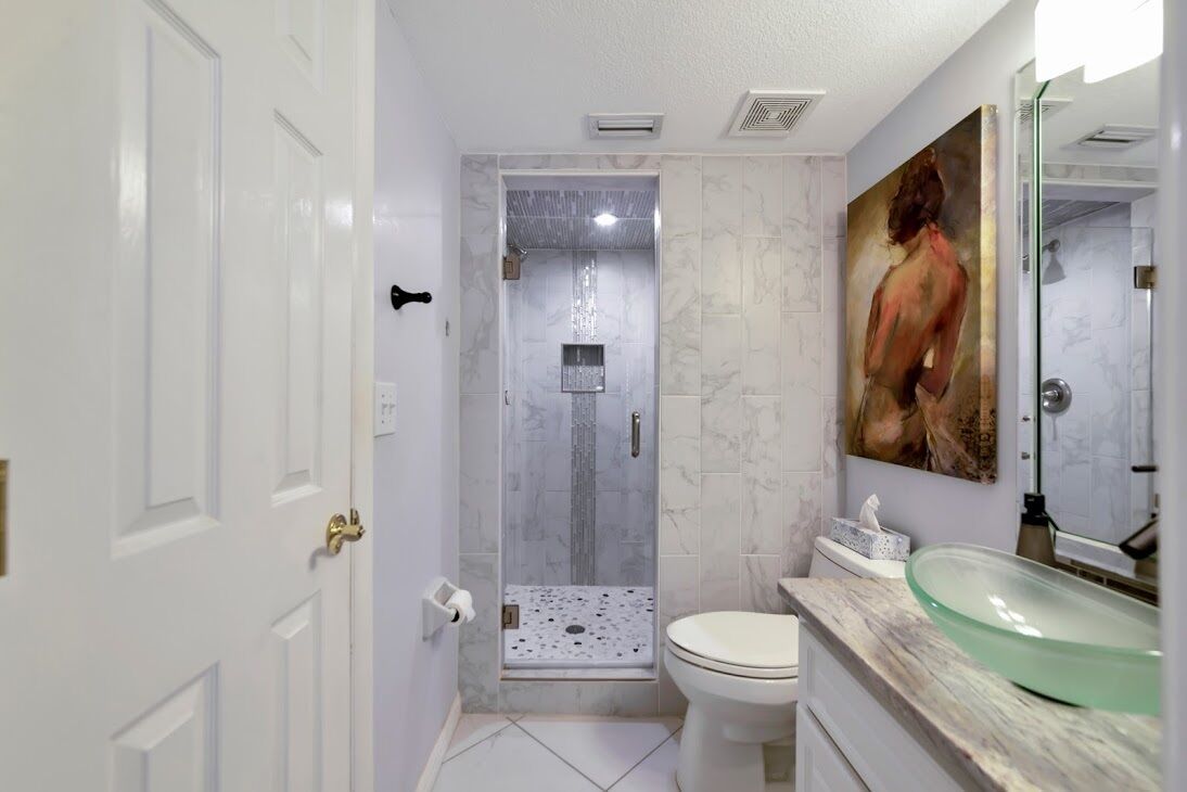 A bathroom with a glass-enclosed shower, a white toilet, and a marble-tiled wall.