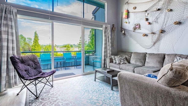 Een ruime woonkamer met een grote schuifpui naar een buitenruimte, een grijze bank, een paarse fauteuil en een salontafel.