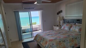 Een slaapkamer met een bed, nachtkastje, lamp, plafondventilator en uitzicht op de oceaan door een schuifdeur.