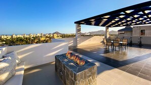 A rooftop terrace with a stone fire feature, outdoor seating, and a view of the cityscape. - 2 Bedroom Condo a few steps from Médano Beach (Los Cabos)