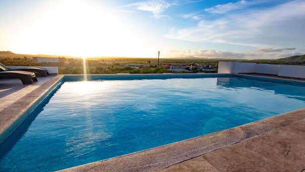 A swimming pool with a clear view of the surrounding landscape and a sunset in the background. - 2 Bedroom Condo a few steps from Médano Beach (Los Cabos)