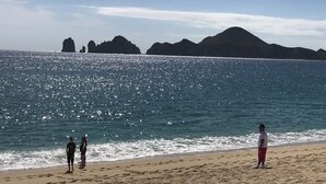 A beach with clear water, rocky formations in the distance, and a sandy shore. - 2 Bedroom Condo a few steps from Médano Beach (Los Cabos)