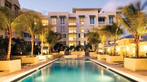 Ein Hotel mit Pool, umgeben von Palmen und einer gut beleuchteten Fassade.