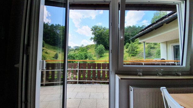 A room with a sliding glass door leading to an outdoor patio area with a view of a green landscape and a wooden fence.