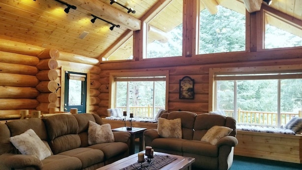 A log cabin interior with a large sofa, a smaller sofa, and a coffee table. There are large windows with a view of trees. - PRICES REDUCED !  Luxury upscale cabin, quiet cul-de-sac, free Wi-Fi (Duck Creek Village)
