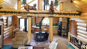 A log cabin interior with a central wood-burning stove, wooden furniture, and decorative animal figures on the ceiling. - PRICES REDUCED !  Luxury upscale cabin, quiet cul-de-sac, free Wi-Fi (Duck Creek Village)