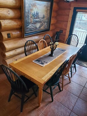 Uma mesa de jantar de madeira com cadeiras, um quadro de uma cena de inverno e uma janela com persianas.